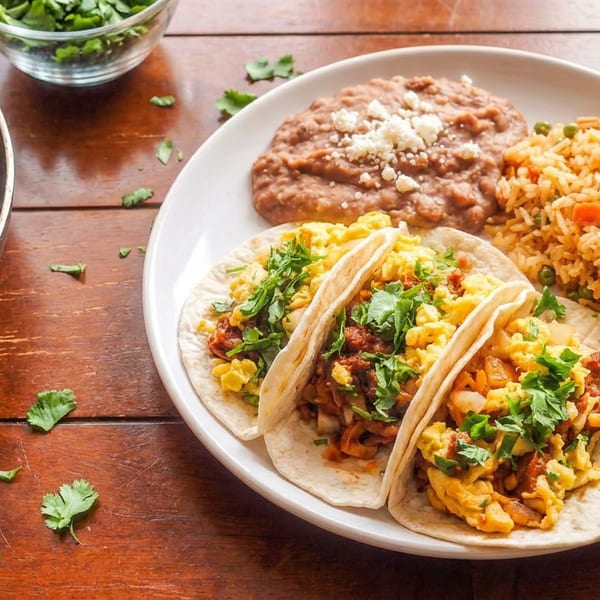 Mexican breakfast plate with egg tacos, refried beans, Mexican rice, chorizo-potato skillet, salsa, and fresh cilantro.